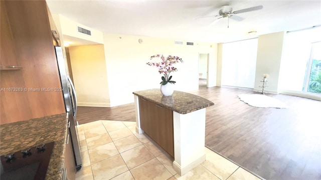 kitchen with stovetop, light hardwood / wood-style flooring, dark stone countertops, a center island, and ceiling fan