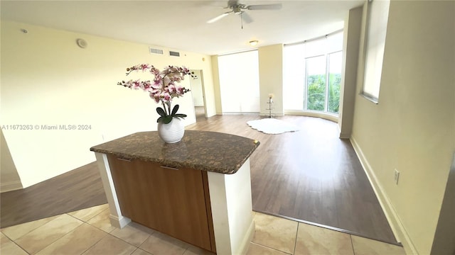 interior space with dark stone countertops, a kitchen island, light wood-type flooring, and ceiling fan