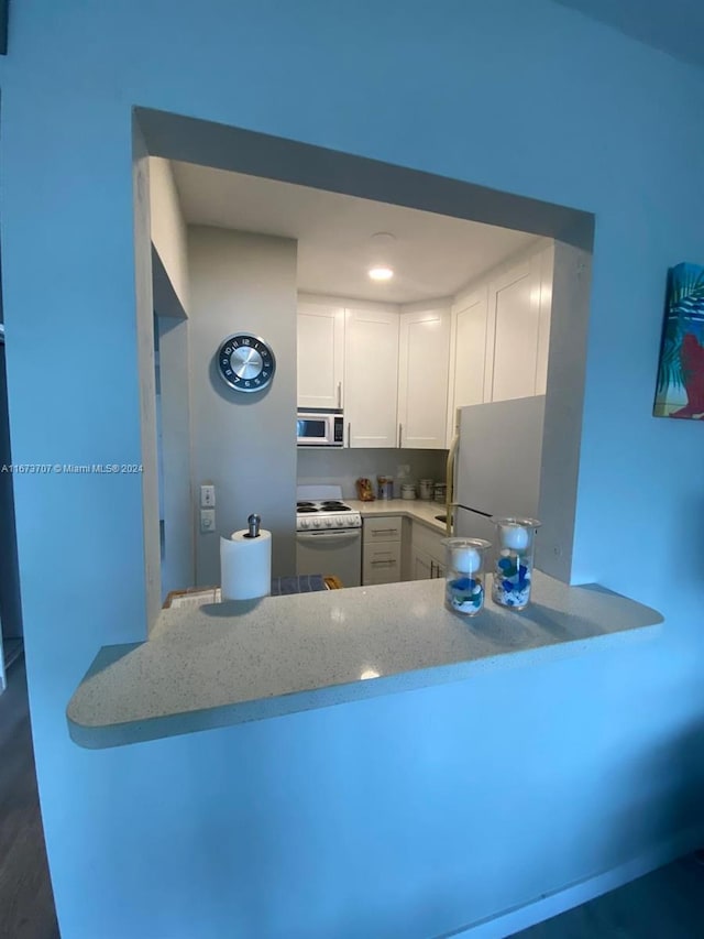 kitchen featuring light stone counters, white cabinets, dark wood-type flooring, white appliances, and kitchen peninsula