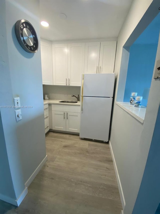 kitchen featuring sink, light hardwood / wood-style flooring, white fridge, and white cabinetry