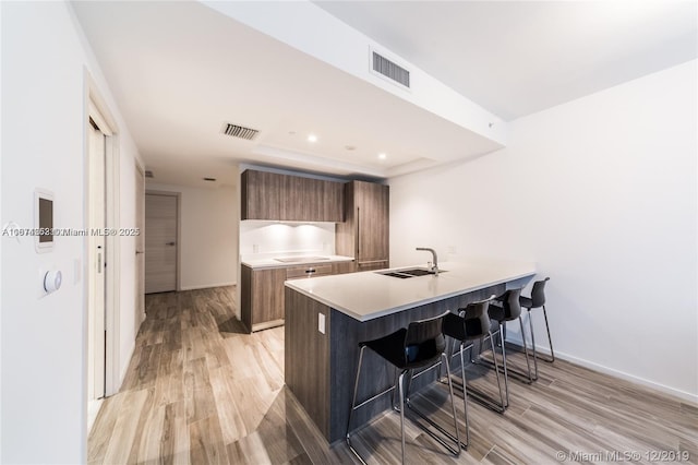 kitchen with black electric stovetop, a kitchen breakfast bar, sink, and light hardwood / wood-style flooring