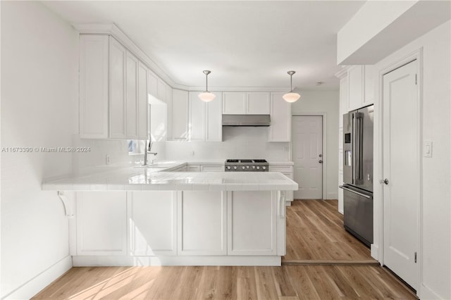 kitchen with kitchen peninsula, stainless steel appliances, sink, pendant lighting, and light hardwood / wood-style flooring