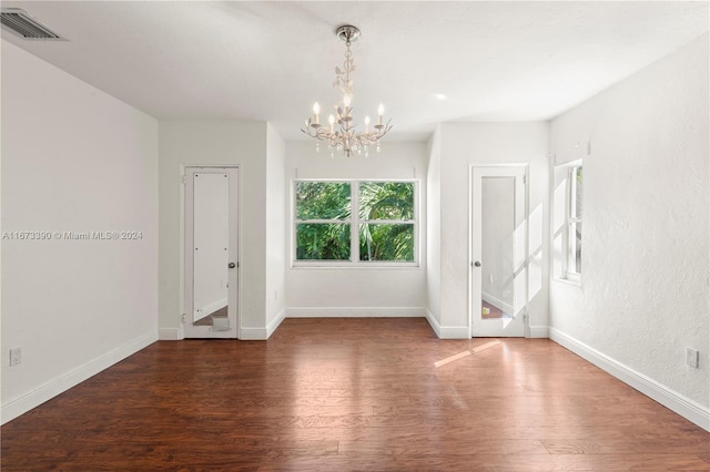 spare room with a chandelier and dark wood-type flooring