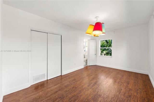 unfurnished bedroom with dark hardwood / wood-style floors, ensuite bath, and a closet