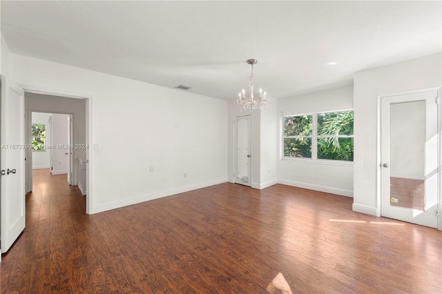 empty room with a notable chandelier and dark wood-type flooring