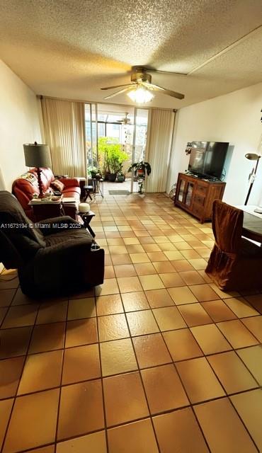 living area with a textured ceiling, light tile patterned floors, and ceiling fan