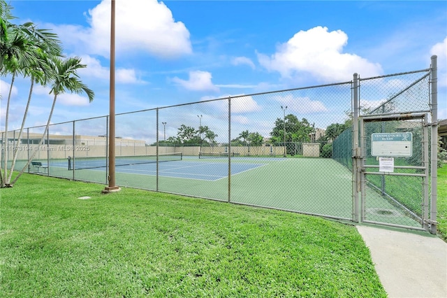 view of tennis court featuring a gate, a lawn, and fence