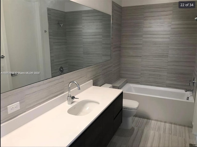 full bathroom featuring toilet, tile walls, vanity, and tiled shower / bath