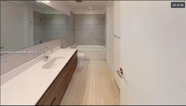 full bathroom featuring hardwood / wood-style floors, tiled shower / bath combo, vanity, and toilet