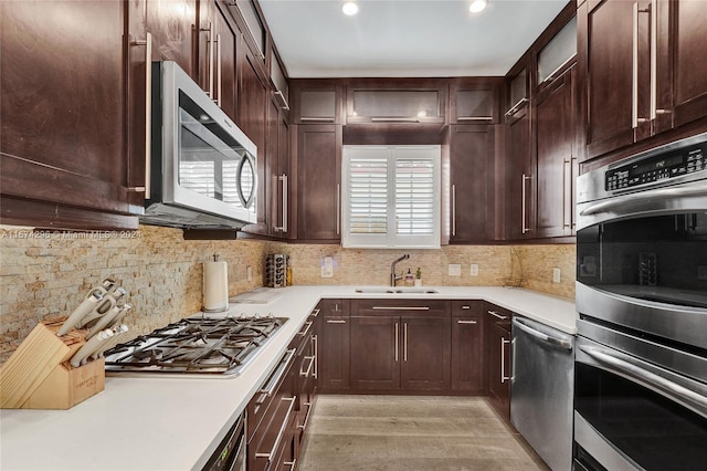 kitchen with dark brown cabinetry, sink, backsplash, appliances with stainless steel finishes, and light wood-type flooring