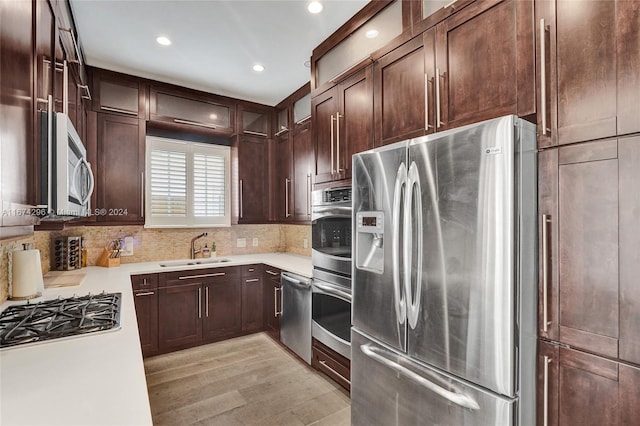 kitchen featuring light wood-type flooring, dark brown cabinetry, sink, decorative backsplash, and appliances with stainless steel finishes