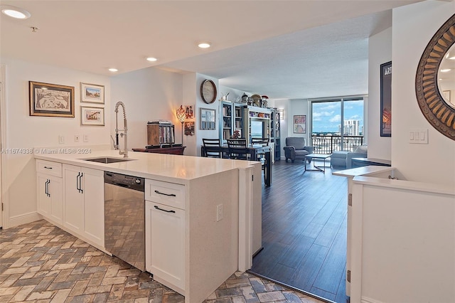 kitchen with a peninsula, stainless steel dishwasher, a sink, and white cabinetry