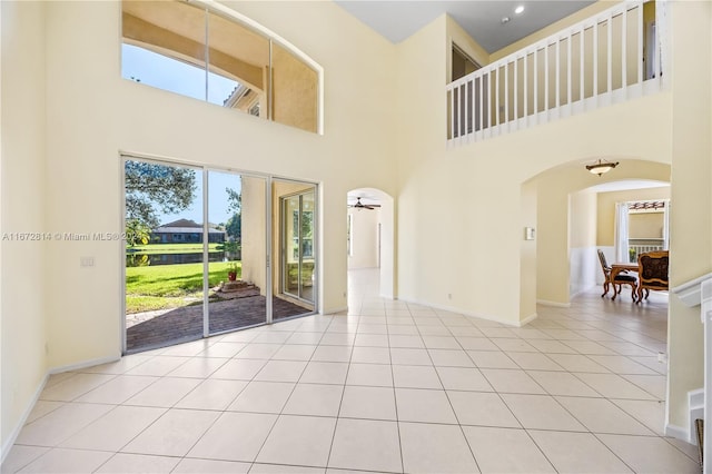 spare room with a towering ceiling, light tile patterned floors, and ceiling fan