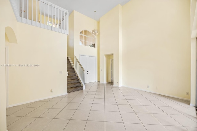 spare room with a towering ceiling, light tile patterned flooring, and a notable chandelier