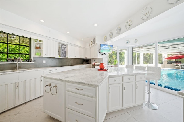 kitchen with a healthy amount of sunlight, a center island, light stone counters, and white cabinetry