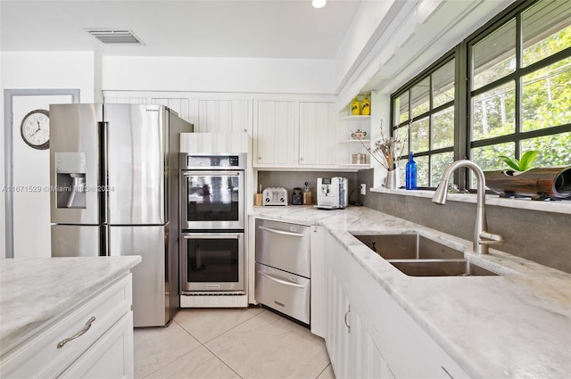 kitchen featuring sink, appliances with stainless steel finishes, light stone counters, and white cabinetry