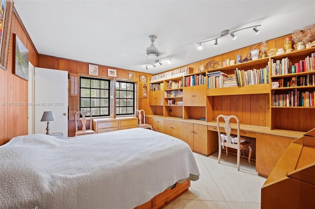 bedroom featuring built in desk, ceiling fan, rail lighting, wooden walls, and light tile patterned floors