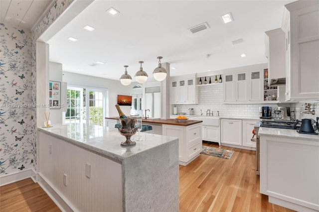 kitchen with light stone countertops, light wood-type flooring, a kitchen island, pendant lighting, and white cabinetry