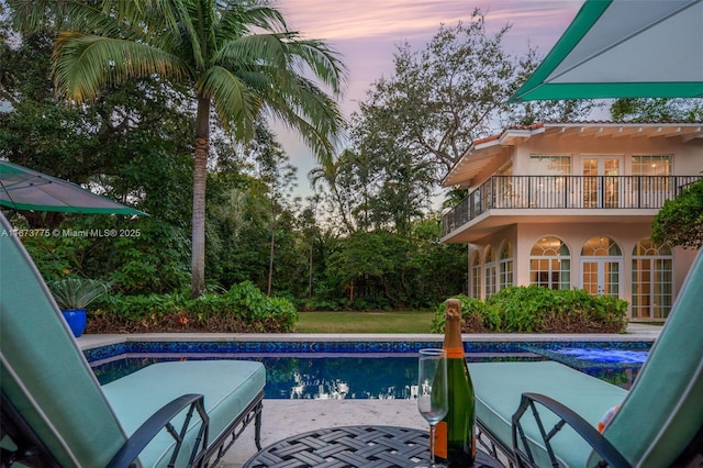 pool at dusk featuring french doors and a patio