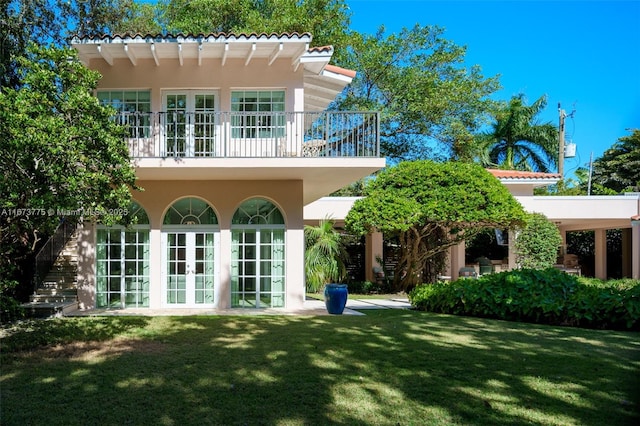 rear view of property with a lawn, a balcony, and french doors