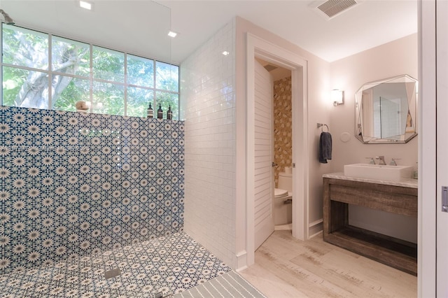 bathroom featuring hardwood / wood-style floors, vanity, toilet, and tiled shower