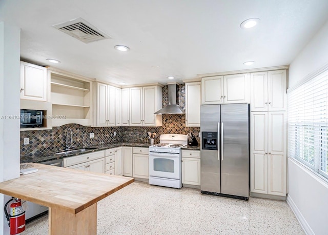 kitchen featuring kitchen peninsula, sink, wall chimney exhaust hood, stainless steel fridge with ice dispenser, and white range with gas cooktop