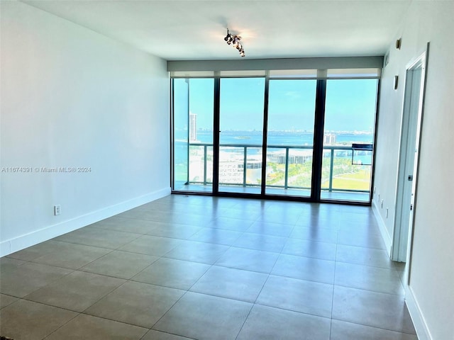 unfurnished room with a wall of windows, a water view, and tile patterned floors