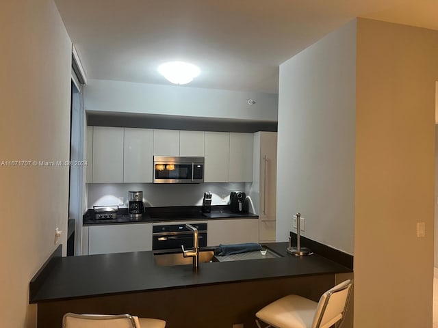 kitchen with white cabinets, a breakfast bar area, appliances with stainless steel finishes, and kitchen peninsula