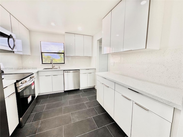 kitchen featuring appliances with stainless steel finishes, tasteful backsplash, white cabinetry, sink, and light stone countertops