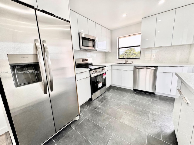 kitchen with sink, dark tile patterned floors, appliances with stainless steel finishes, white cabinets, and decorative backsplash