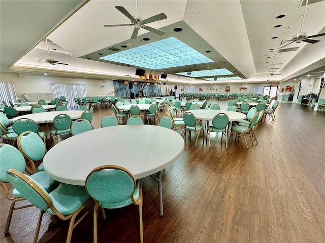 dining space with ceiling fan, a raised ceiling, and hardwood / wood-style floors