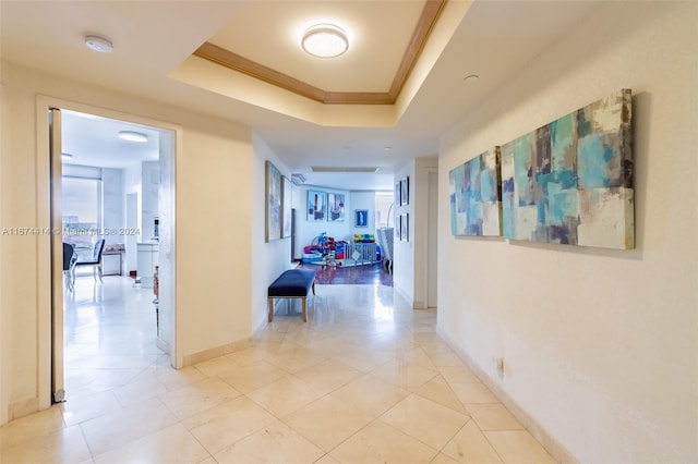 corridor featuring light tile patterned floors, baseboards, a raised ceiling, and crown molding