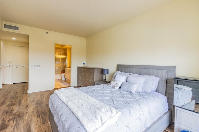 bedroom with ensuite bath, wood finished floors, and visible vents