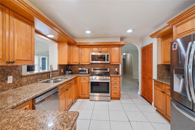 kitchen featuring sink, appliances with stainless steel finishes, stone countertops, light tile patterned floors, and backsplash