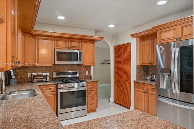 kitchen with sink, decorative backsplash, appliances with stainless steel finishes, light tile patterned floors, and a textured ceiling