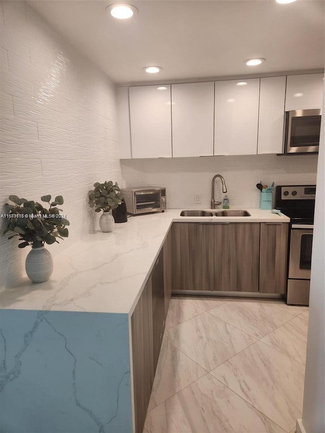 kitchen with light stone counters, appliances with stainless steel finishes, sink, and white cabinetry