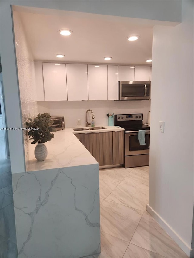 kitchen with light stone counters, sink, stainless steel appliances, and white cabinets