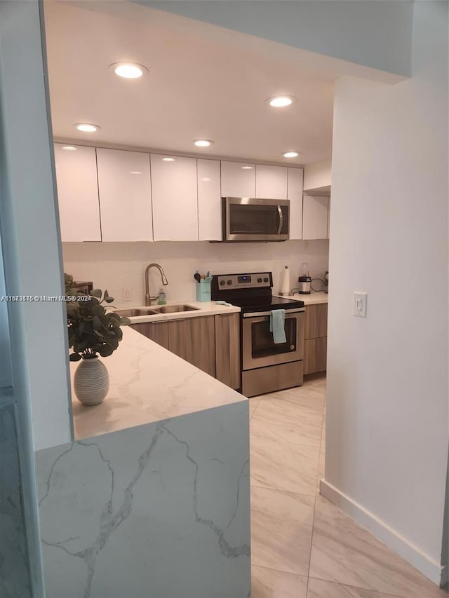 kitchen with appliances with stainless steel finishes, light stone counters, sink, and white cabinets