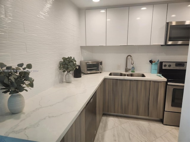 kitchen with light stone counters, white cabinets, stainless steel appliances, and sink