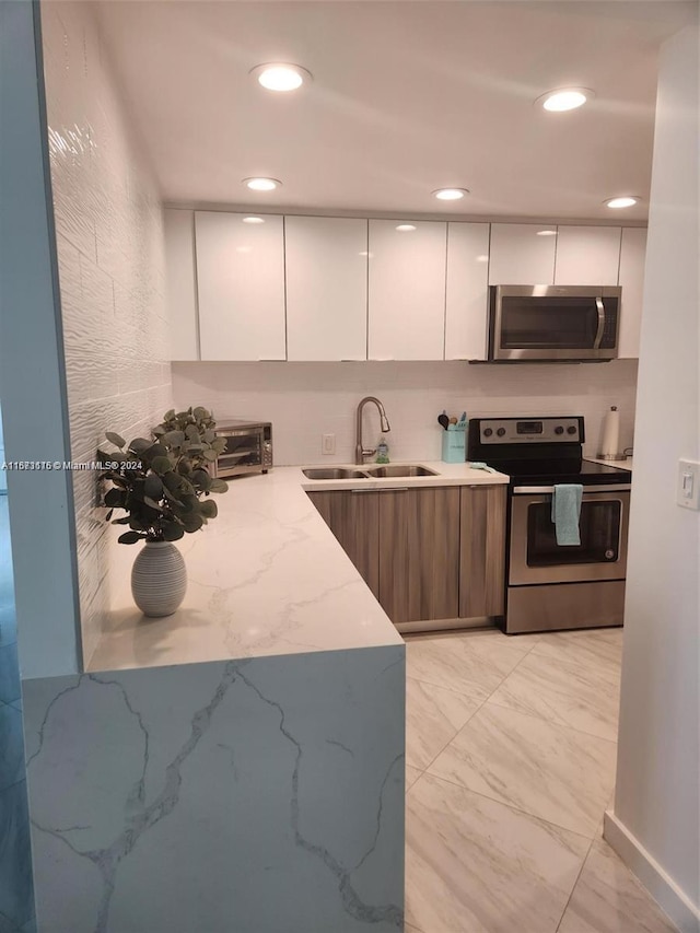 kitchen featuring white cabinets, appliances with stainless steel finishes, light stone counters, and sink