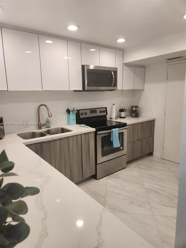 kitchen with white cabinets, stainless steel appliances, sink, and light stone countertops