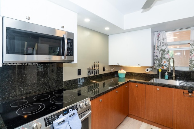 kitchen with white cabinets, sink, dark stone counters, stainless steel appliances, and light wood-type flooring