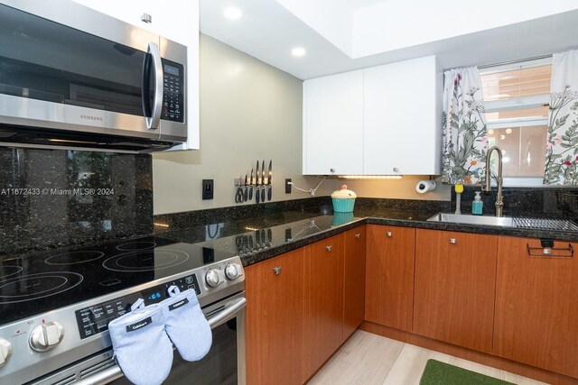 kitchen with stainless steel appliances, dark stone countertops, sink, light hardwood / wood-style floors, and backsplash