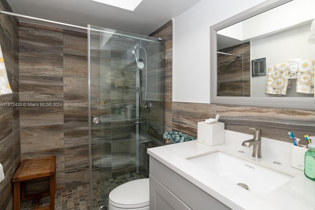 bathroom with vanity, tile walls, toilet, and a shower with shower door