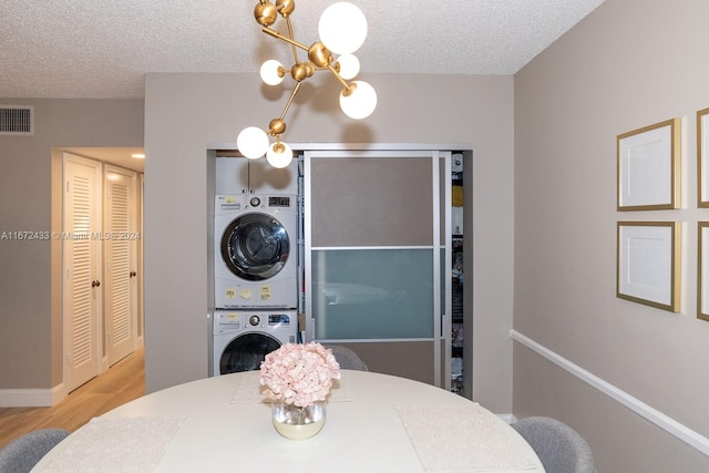 dining area featuring an inviting chandelier, a textured ceiling, light wood-type flooring, and stacked washer / dryer