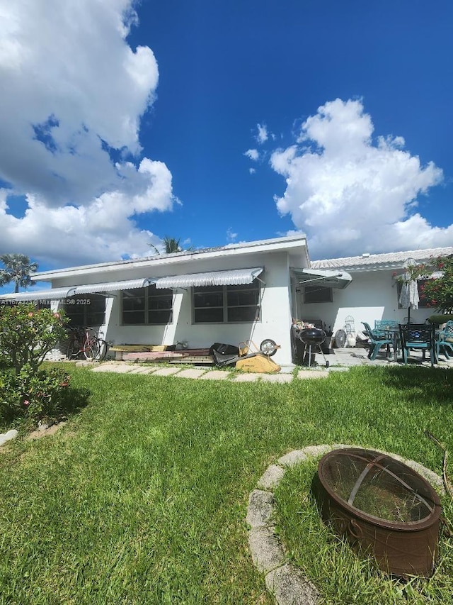 rear view of property with a fire pit, stucco siding, and a yard