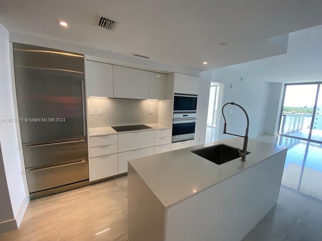 kitchen with a center island with sink, sink, backsplash, black appliances, and white cabinetry