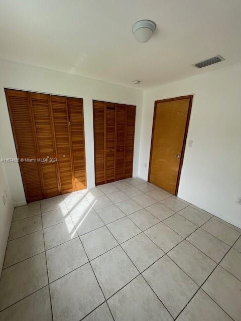 unfurnished bedroom with light tile patterned floors and two closets