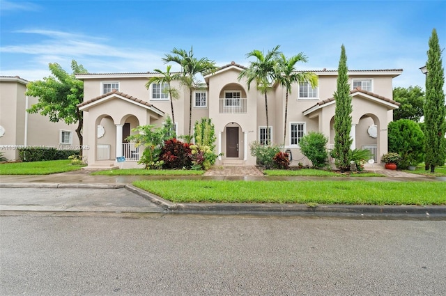 mediterranean / spanish home with stucco siding, a tile roof, and a front lawn