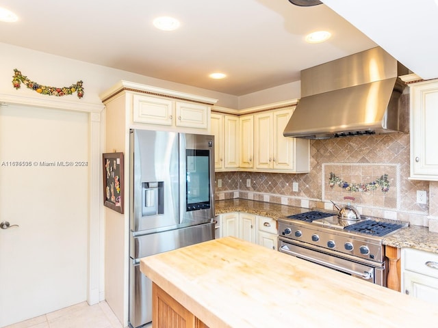 kitchen featuring wall chimney exhaust hood, cream cabinets, appliances with stainless steel finishes, and butcher block counters